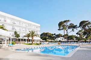 A hotel with a swimming pool, outdoor seating, and palm trees.