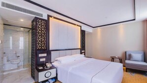 Habitación de hotel con cama, mesita de noche, una silla, zona de ducha y un espejo grande.