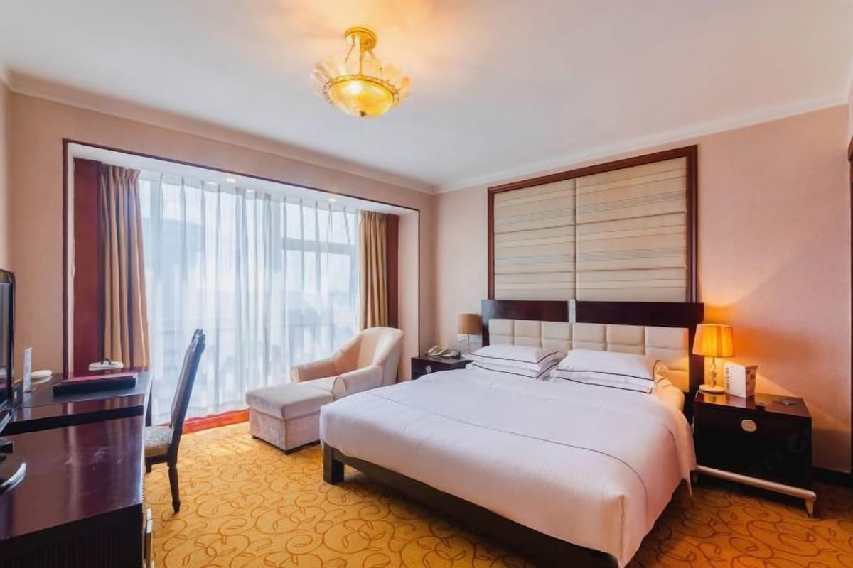 A hotel room with a large bed, a desk, a chair, a television, and a window with curtains.