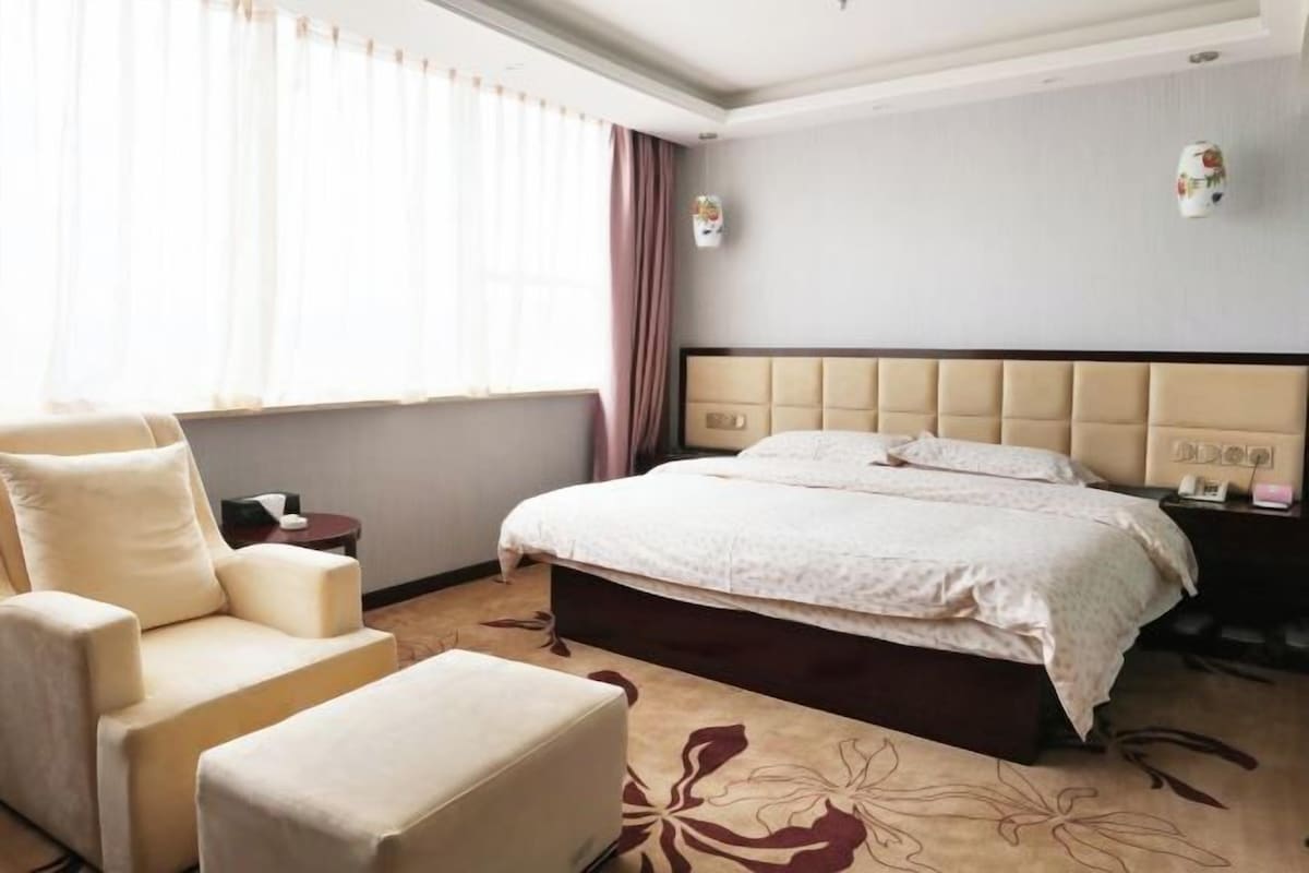 A hotel room with a bed, a chair, a nightstand, and a window with curtains.