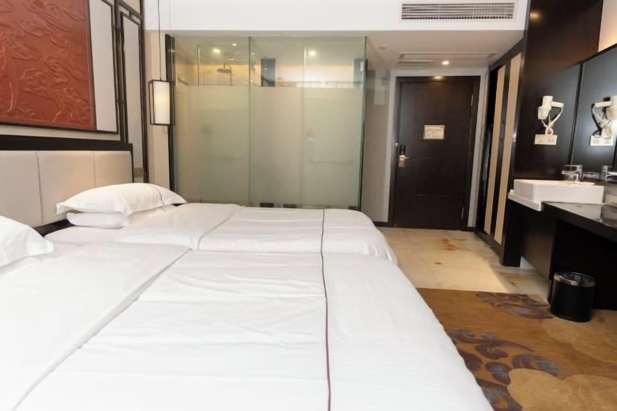 A hotel room with two beds, a bathroom with a glass partition, and a sink.