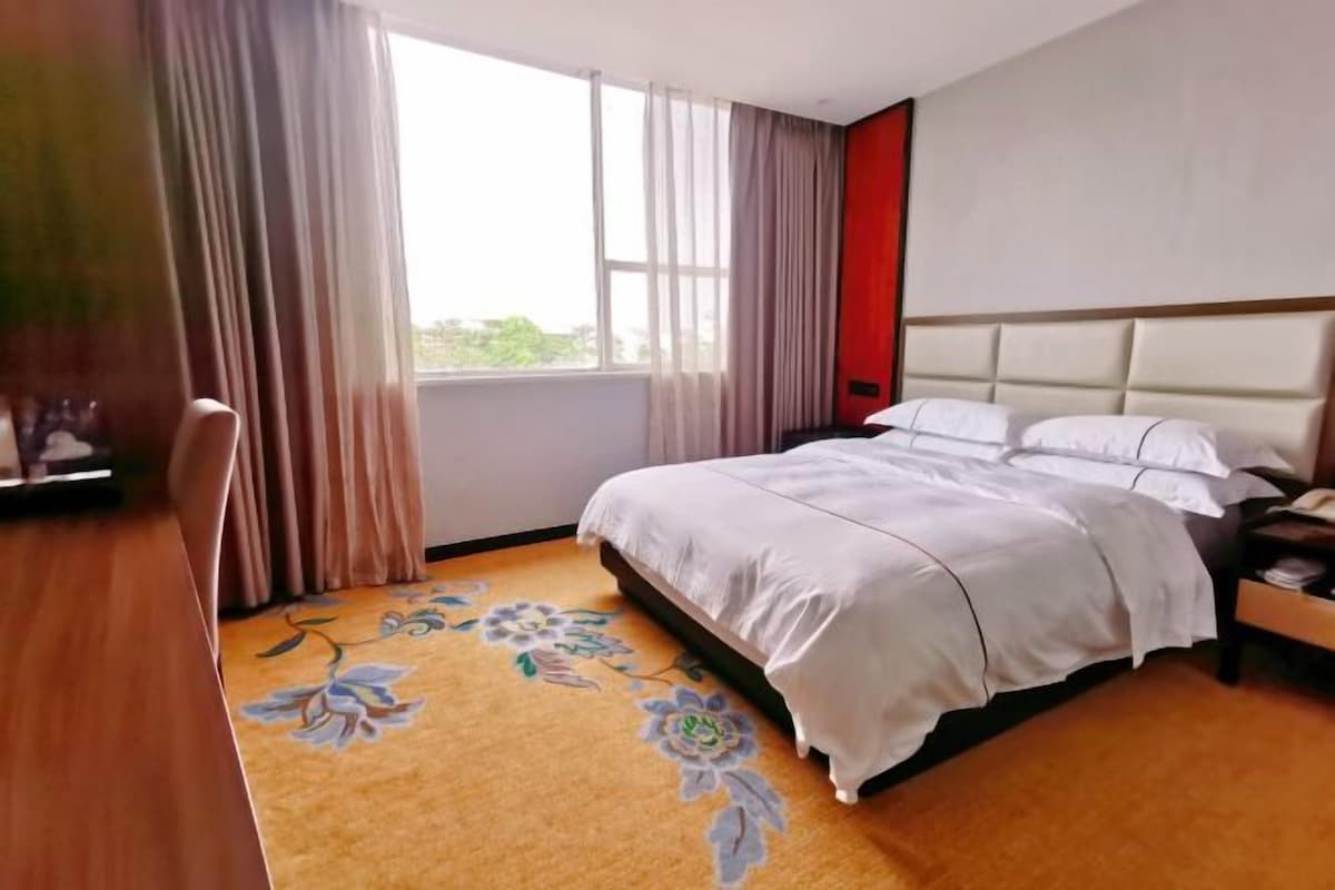 A hotel room with a bed, a desk, and a window with curtains.