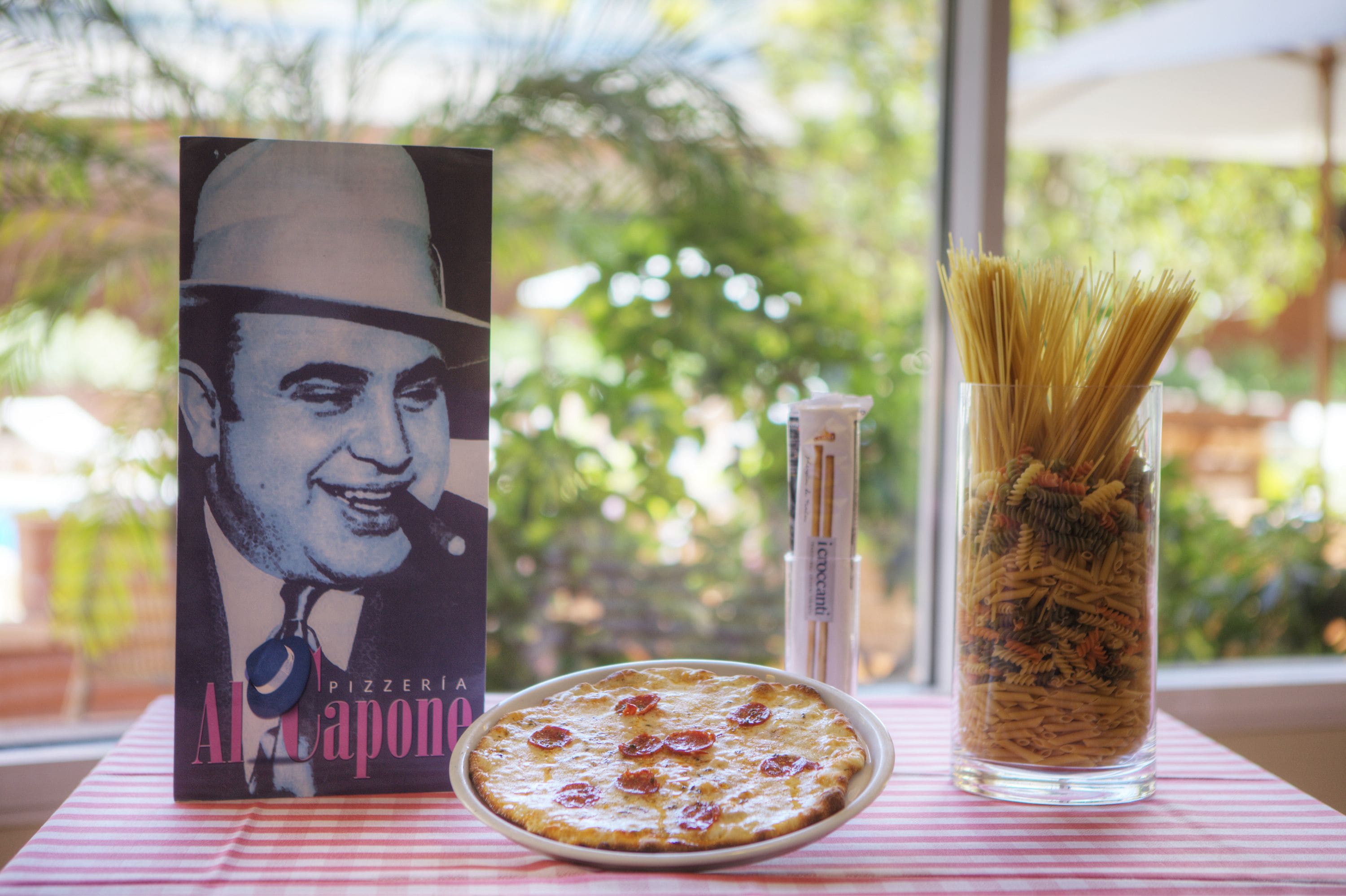 Una mesa con una pizza, un vaso de pasta y un libro titulado "Al Capone Pizzeria".