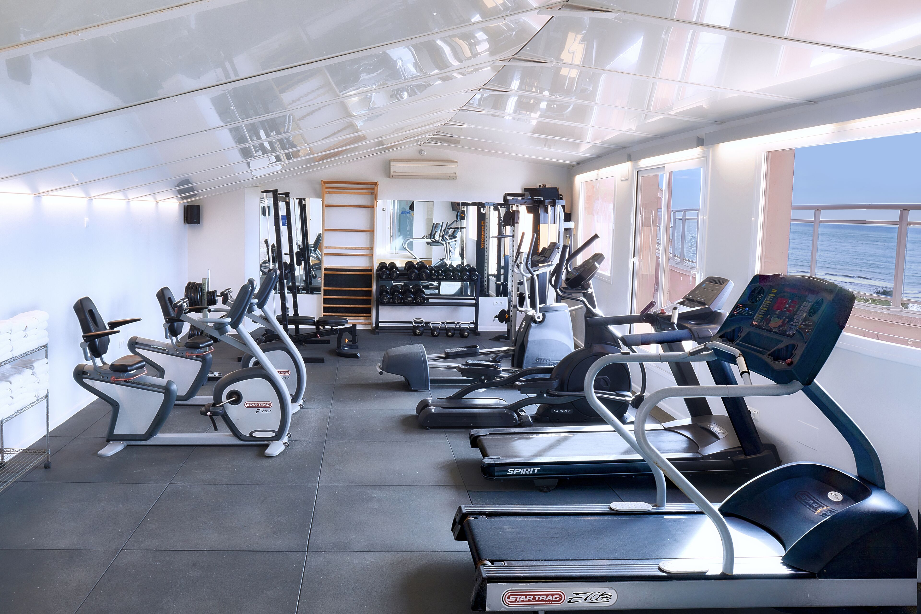 Un gimnasio con diversos equipos de ejercicio, un espejo y una ventana con vista al mar.