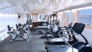 Un gimnasio con diversos equipos de ejercicio, un espejo y una ventana con vista al mar.