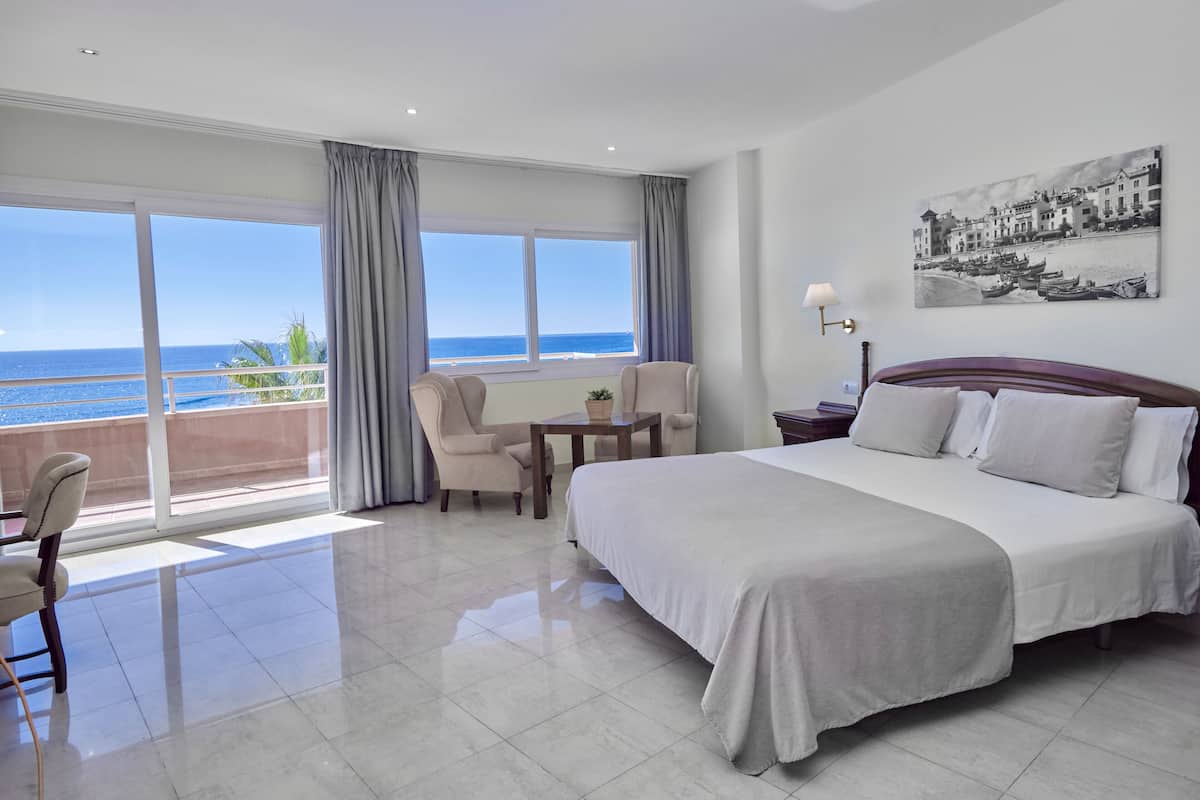 A hotel room with a large bed, a seating area with a table, and a view of the ocean.