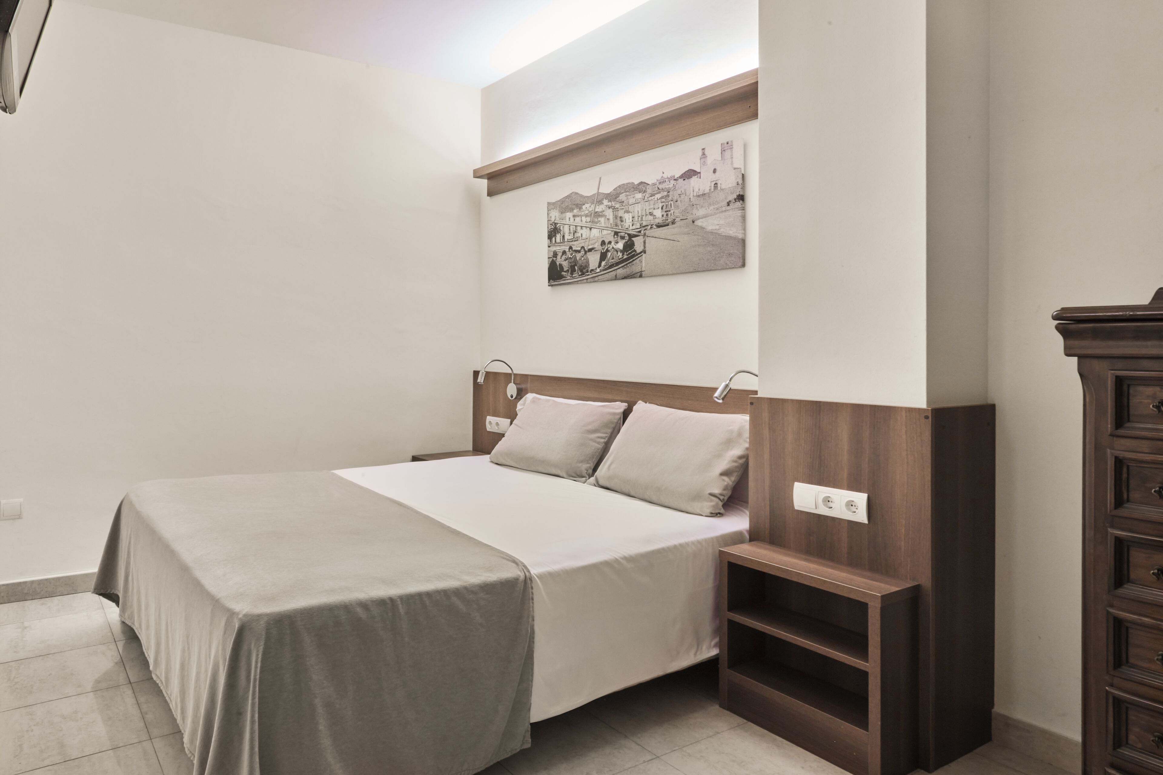 Une chambre à coucher bien rangée, avec un lit, des tables de chevet, une petite table en bois et une étagère fixée au mur.