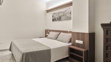 Une chambre à coucher bien rangée, avec un lit, des tables de chevet, une petite table en bois et une étagère fixée au mur.