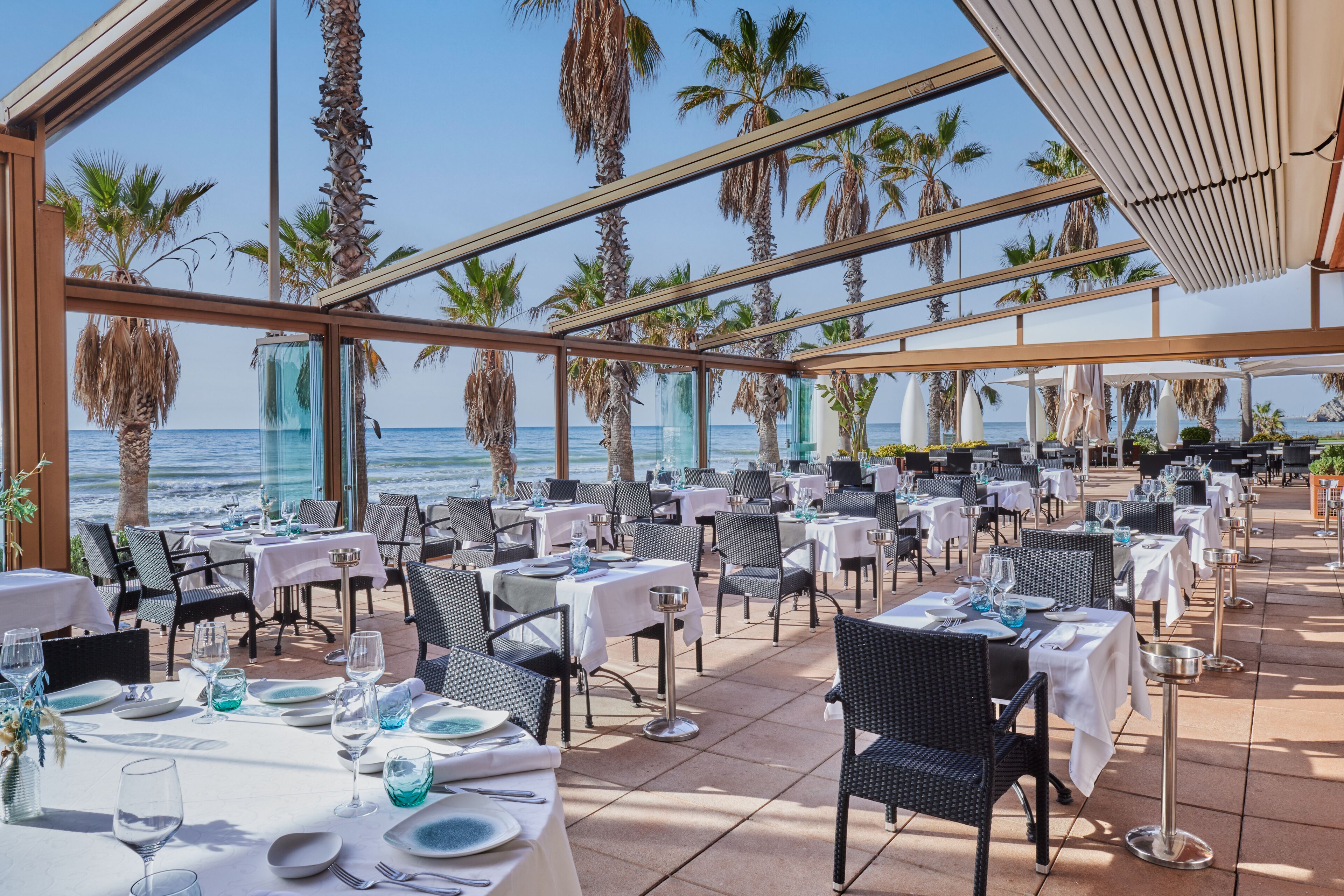 Un espace extérieur aménagé pour les repas, avec des tables dressées pour les clients, offrant une vue sur la mer.