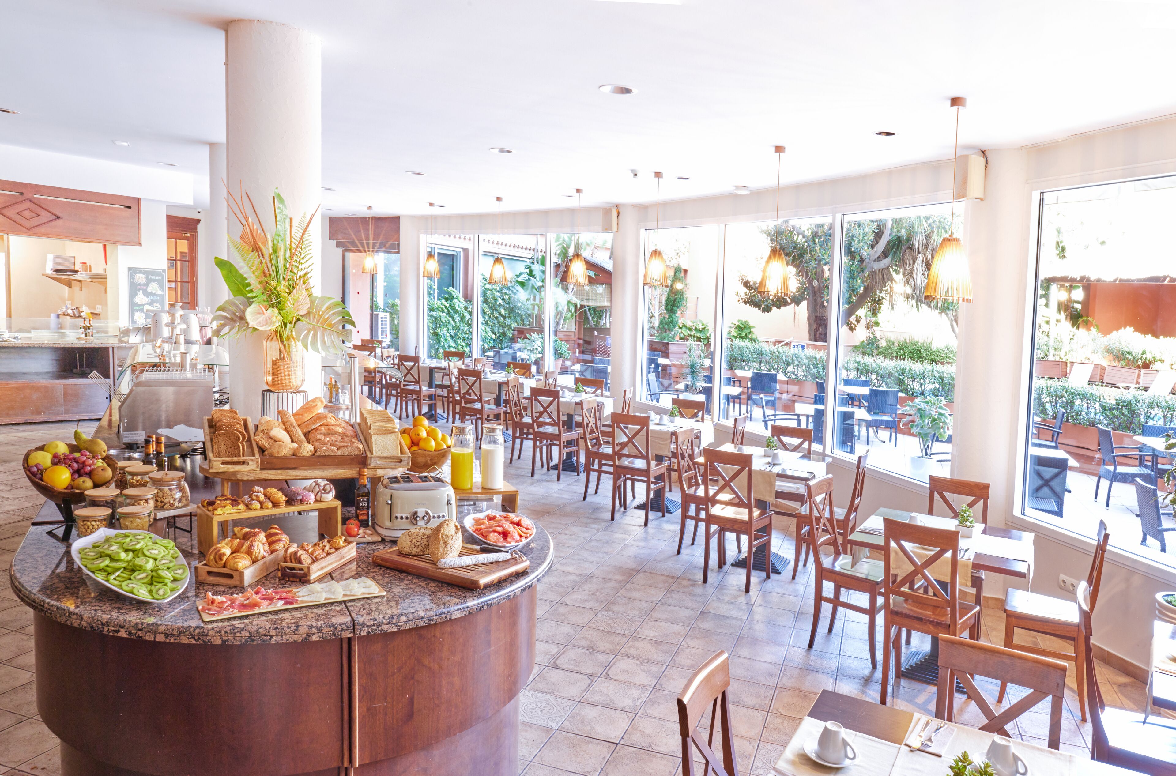 A spacious breakfast area with a central counter filled with various food items and a large window offering a view of the outdoor seating area.
