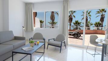Una sala de estar moderna con un sofá, dos sillones, una mesa de centro y una mesa de comedor. Amplias ventanas ofrecen vistas a palmeras y un área de patio.