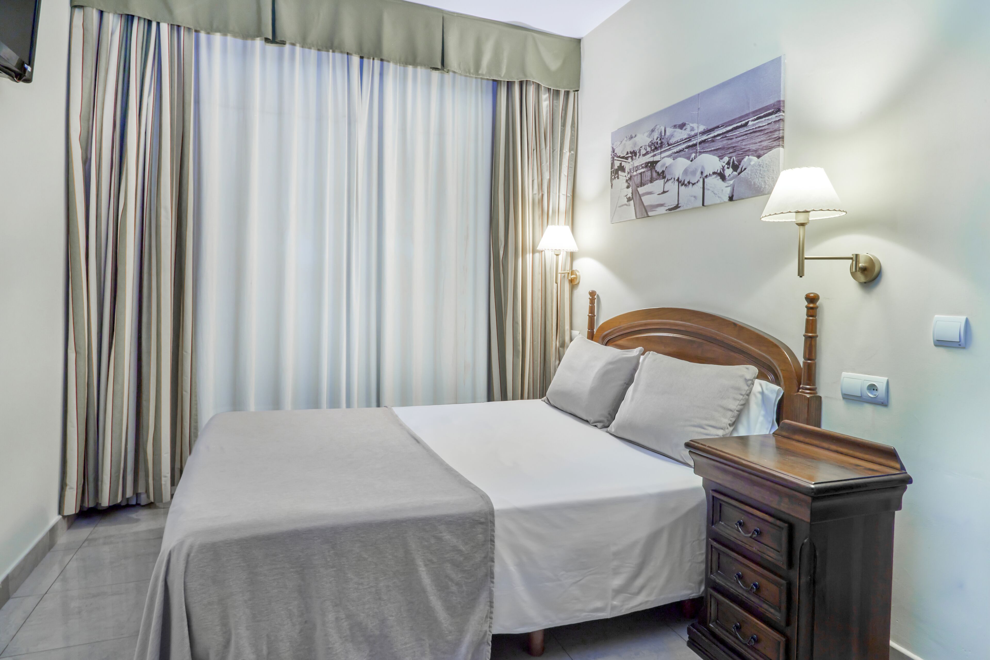 A neatly made bed with a wooden headboard, a bedside table with a lamp, and a wall-mounted picture.