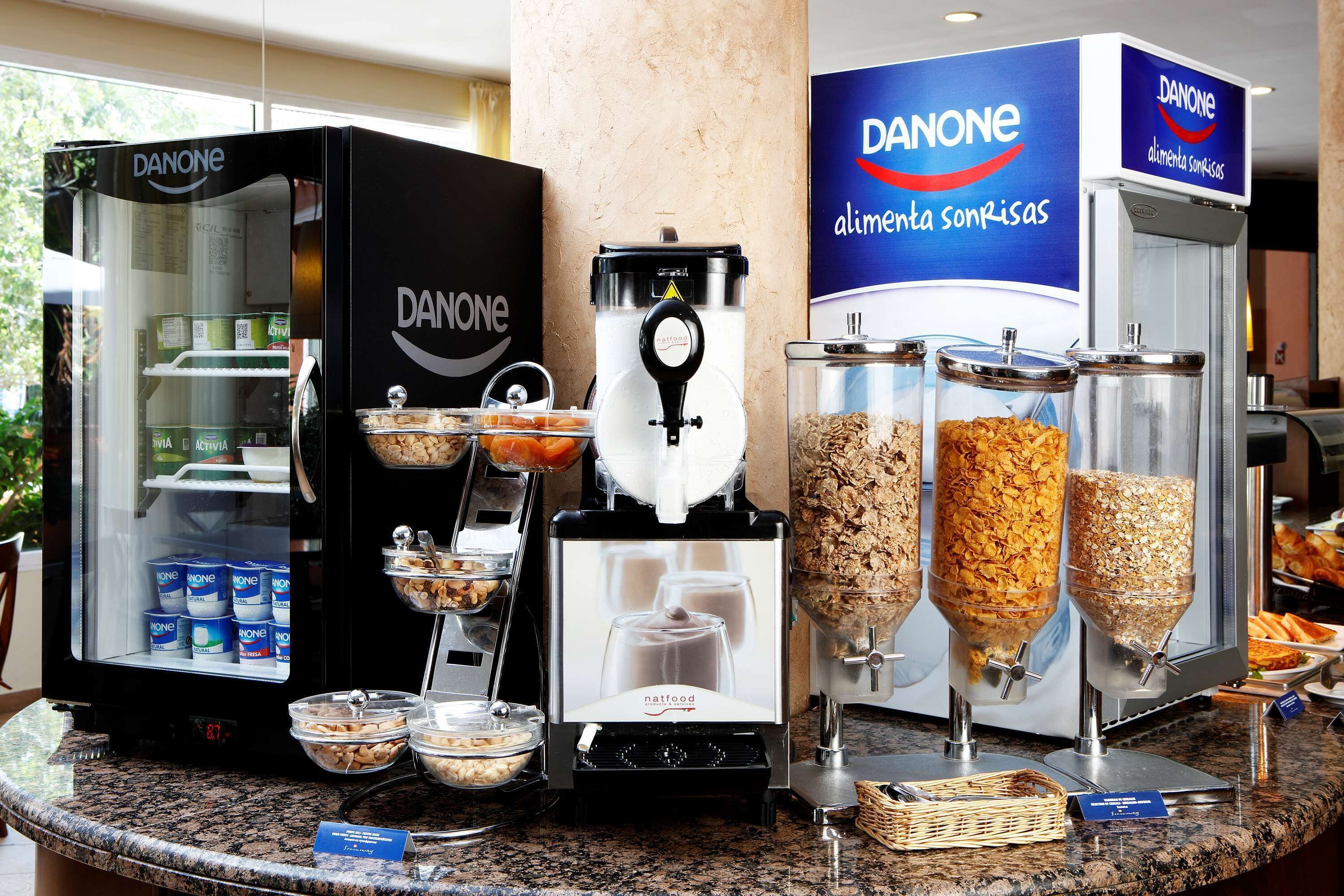 A buffet area with Danone refrigerated display cases, a coffee machine, and various food dispensers.