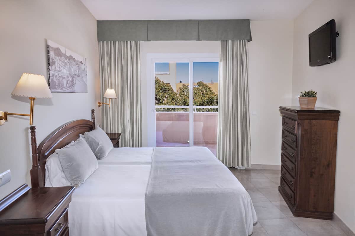 A hotel room with a bed, a dresser, a TV, and a balcony with curtains.