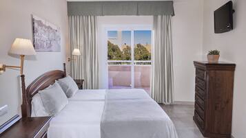 Habitación de hotel con cama, cómoda, televisor y balcón con cortinas.