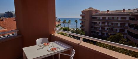 Ein Balkon mit Tisch und Stühlen mit Blick auf einen Strand und ein Hotelgebäude.