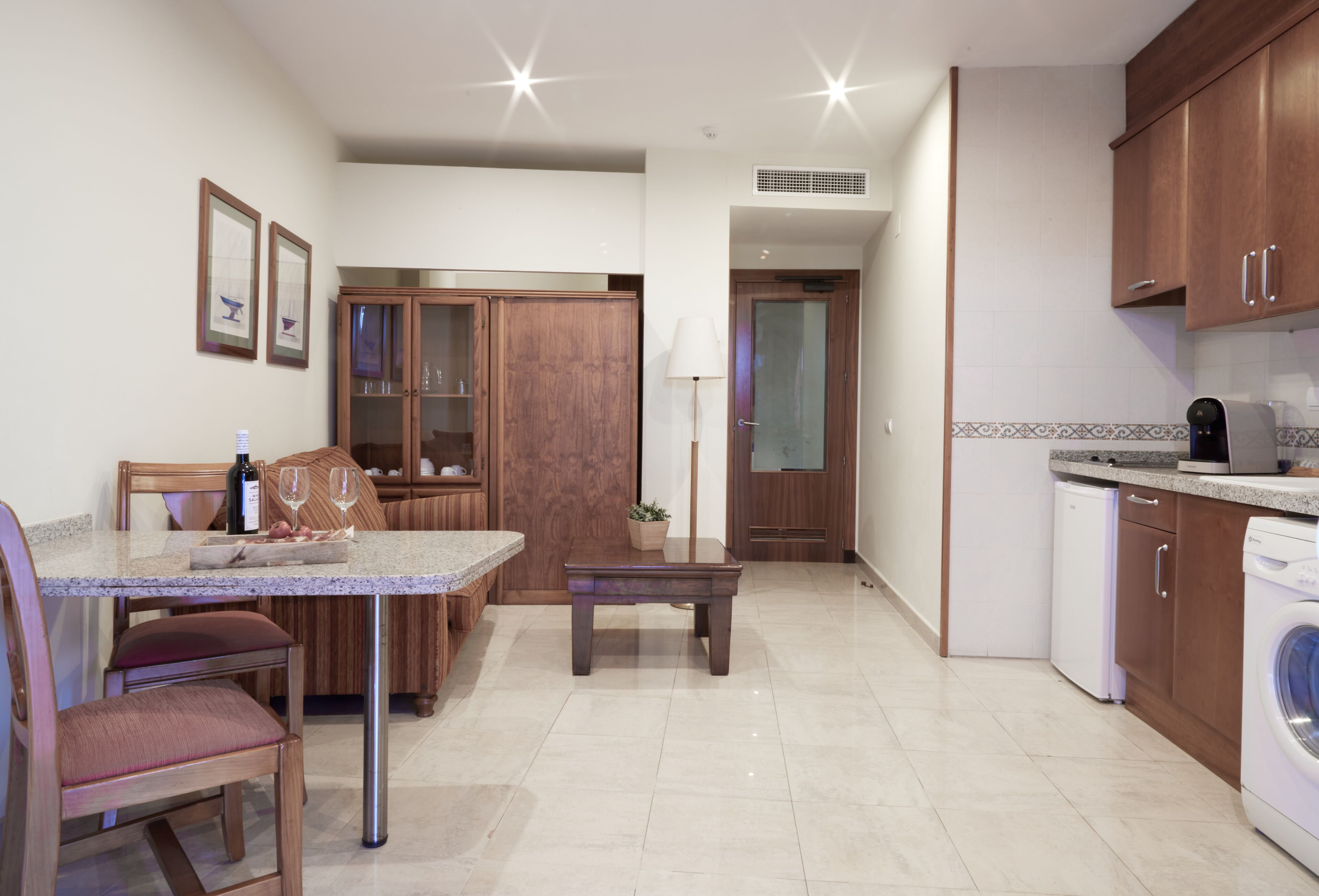 Una cocina moderna con armarios de madera, una zona de comedor con mesa y sillas, y una lavadora.