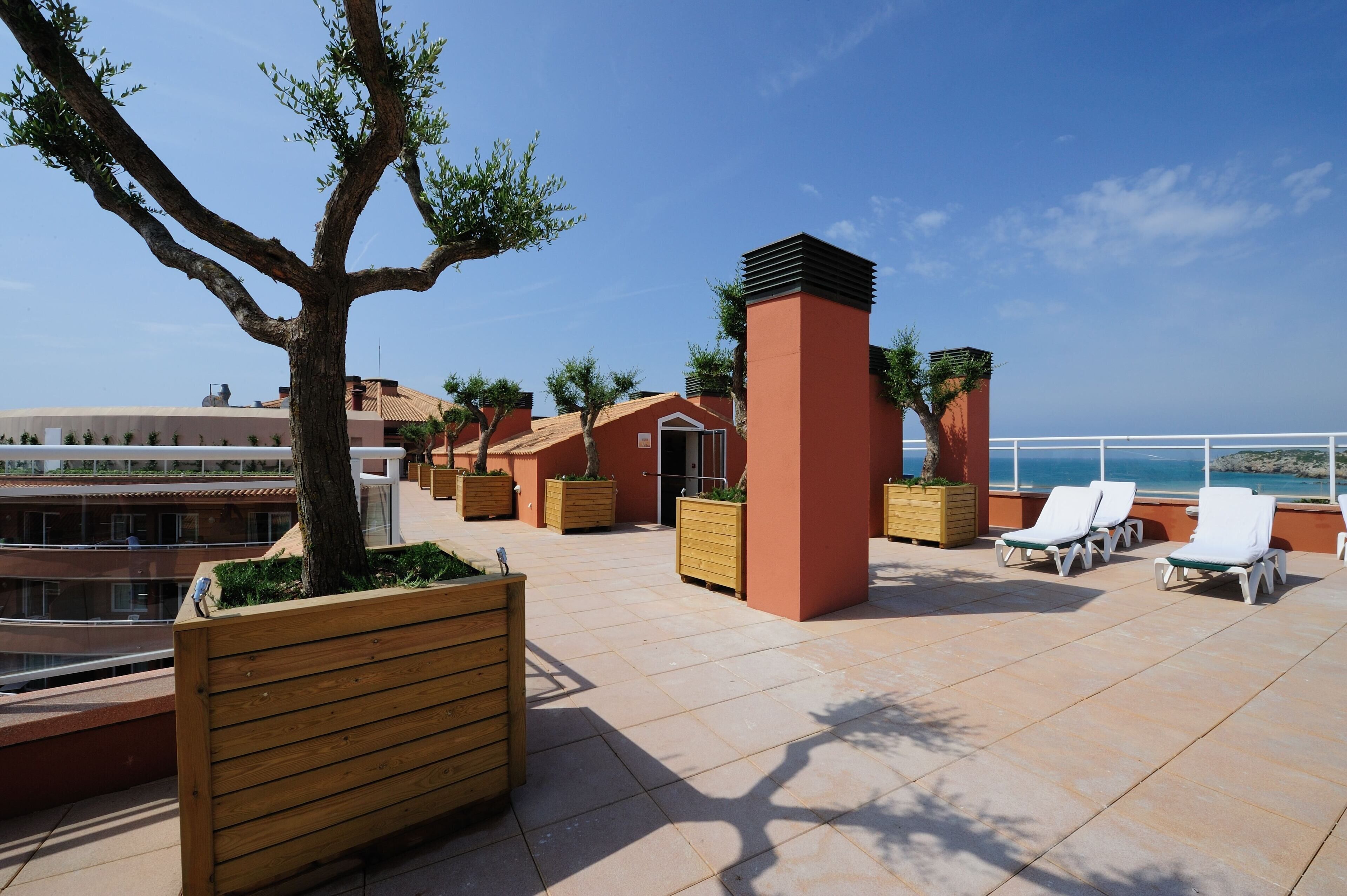 Una terraza en la azotea con macetas de madera, sillones de descanso y vistas al mar.