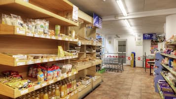 A grocery store with shelves stocked with various food items and a shopping cart near the entrance.