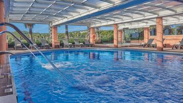 Un área de piscina con agua azul cristalina, sillas de descanso y una estructura techada.