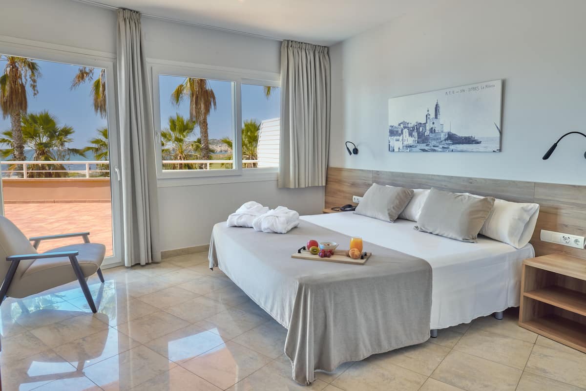 A hotel room with a large bed, a chair, a breakfast tray, and a view of palm trees and a building.
