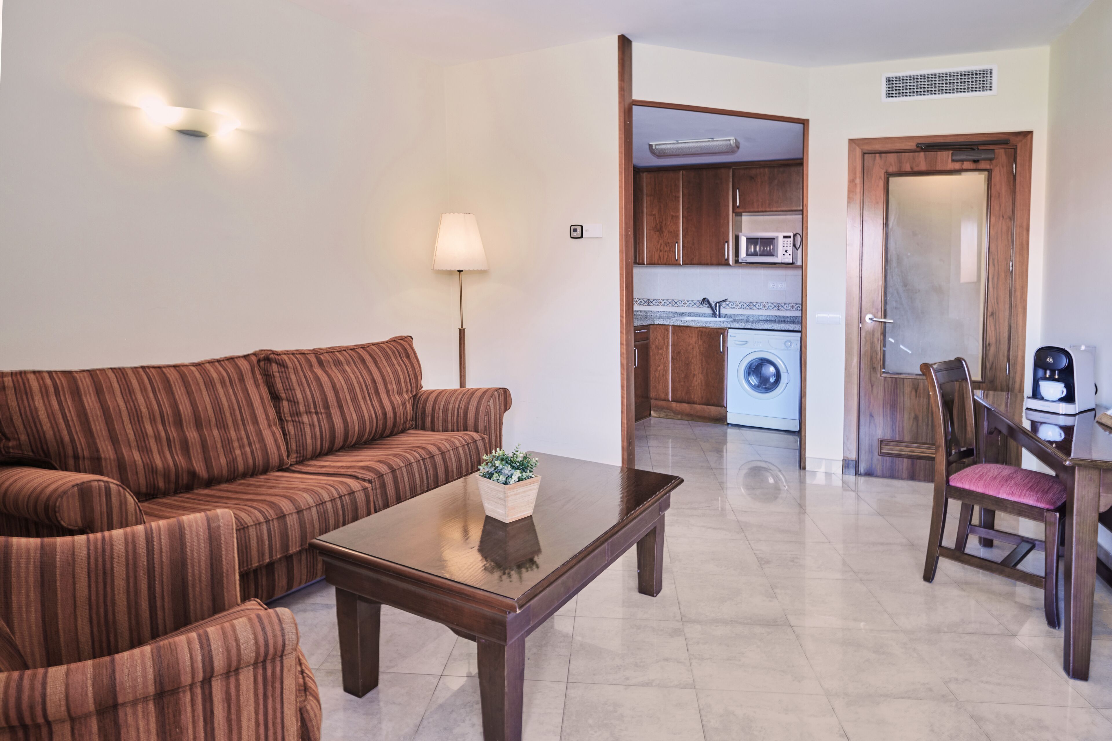 Una sala de estar con un sofá a rayas, una mesa de centro con una planta, y un comedor con una silla y una mesa.