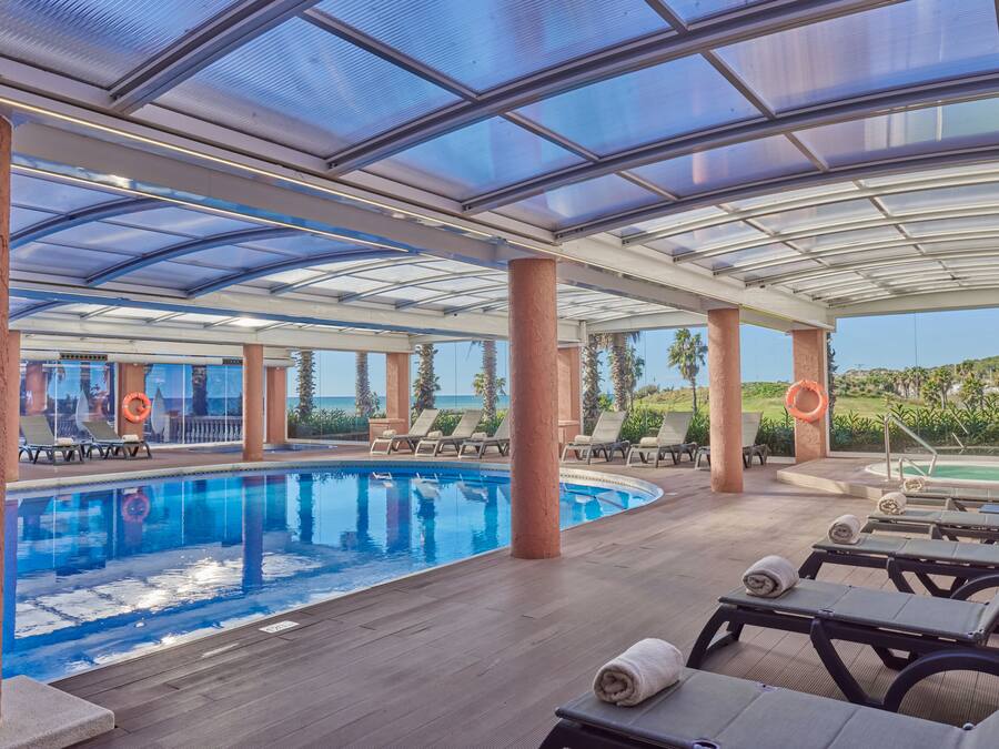 Un área de piscina techada con sillones de descanso y vista al paisaje.