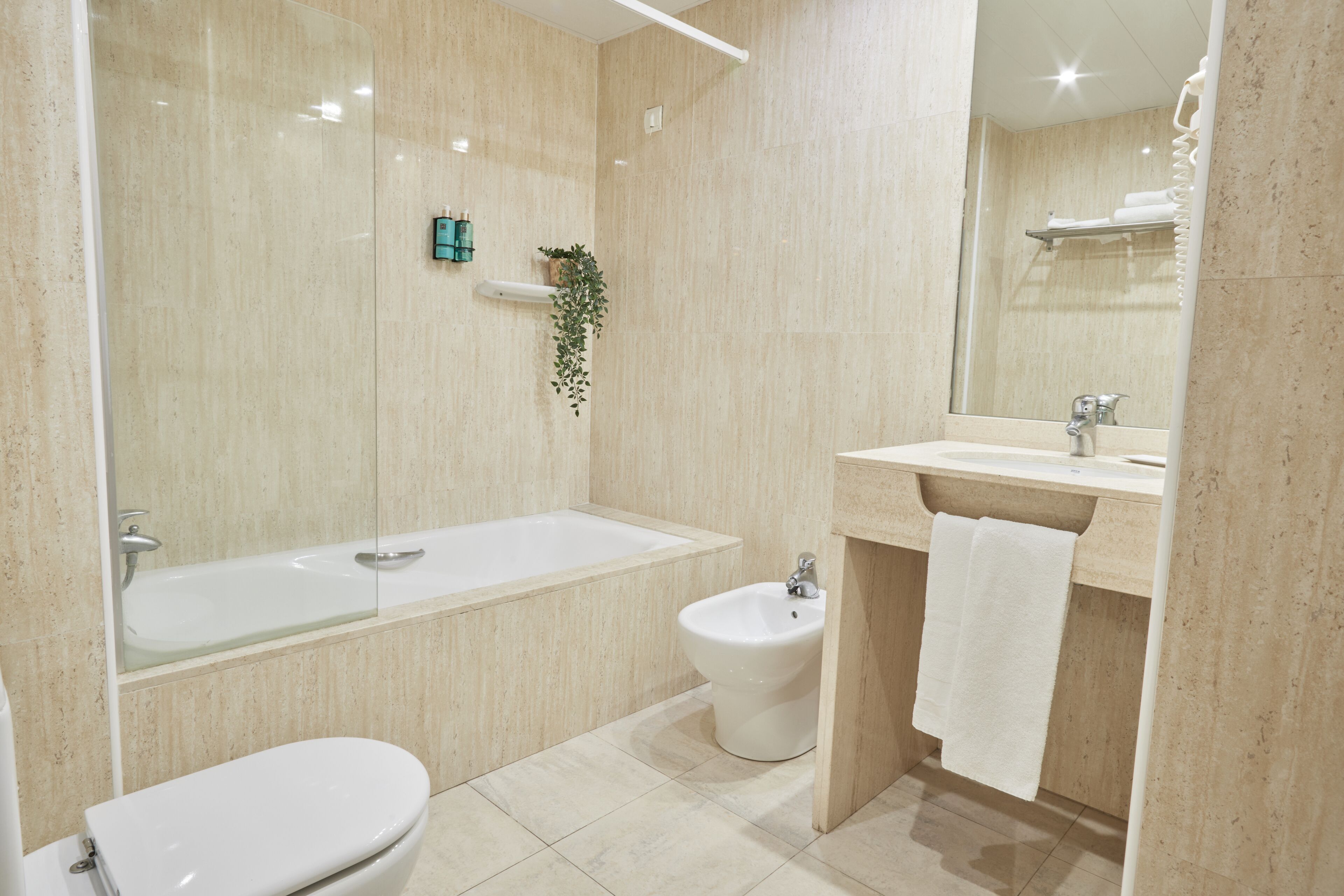 A modern bathroom with a bathtub, toilet, bidet, and a large mirror.