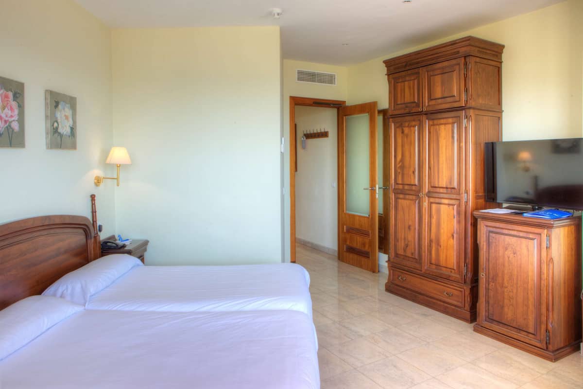 A hotel room with a large bed, wooden wardrobe, a television, and a lamp.