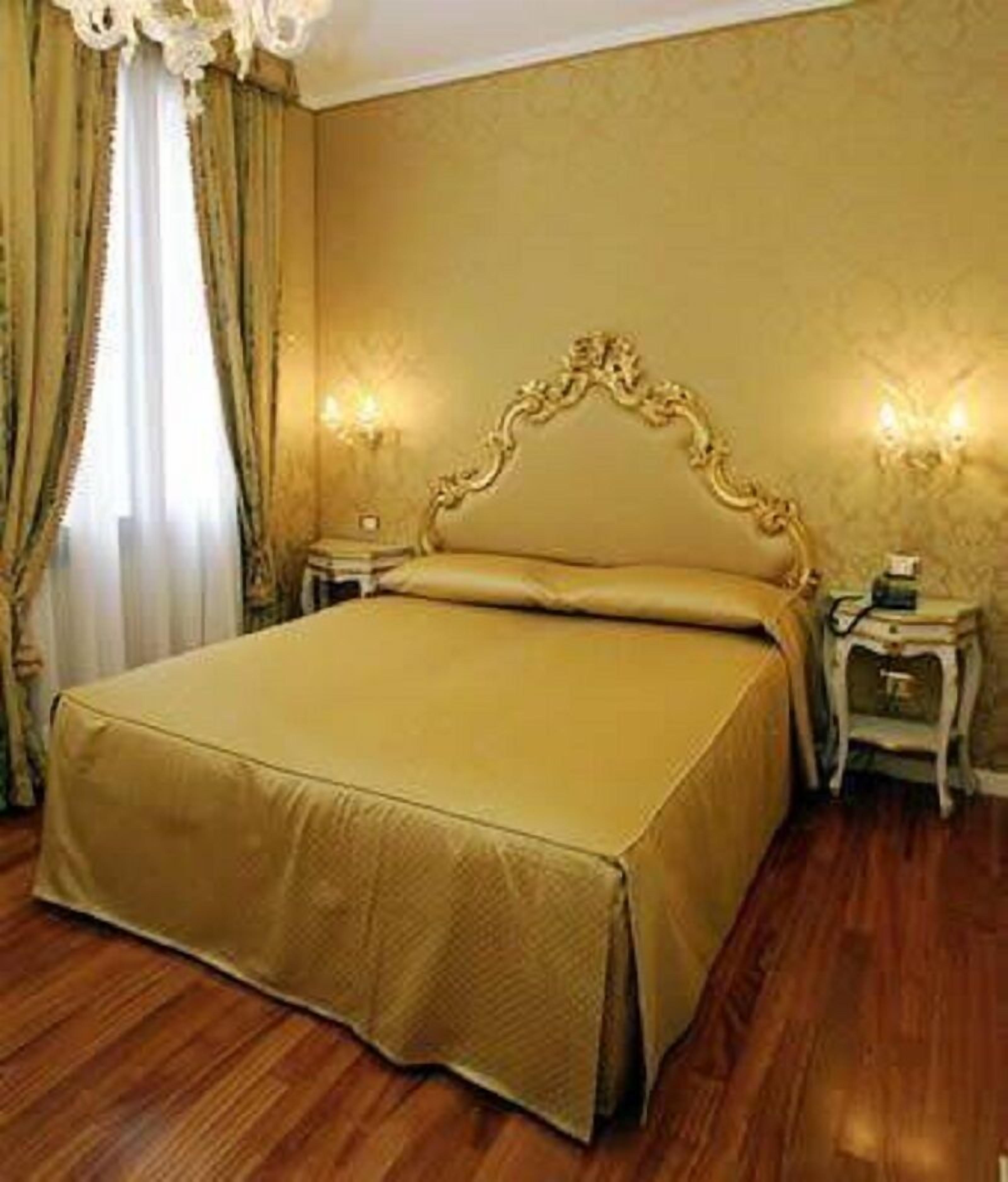 A room with a large bed, wooden flooring, and two bedside tables with lamps.