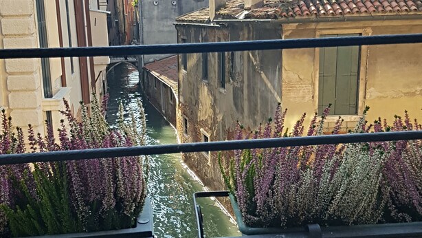 Un canal flanqueado por edificios, con una barandilla en primer plano y cielo despejado.
