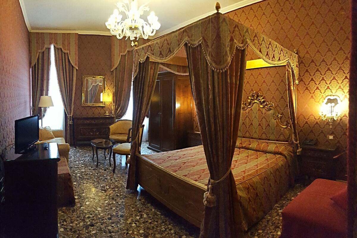 A bedroom with a four-poster bed, a television, a desk, and a chair.