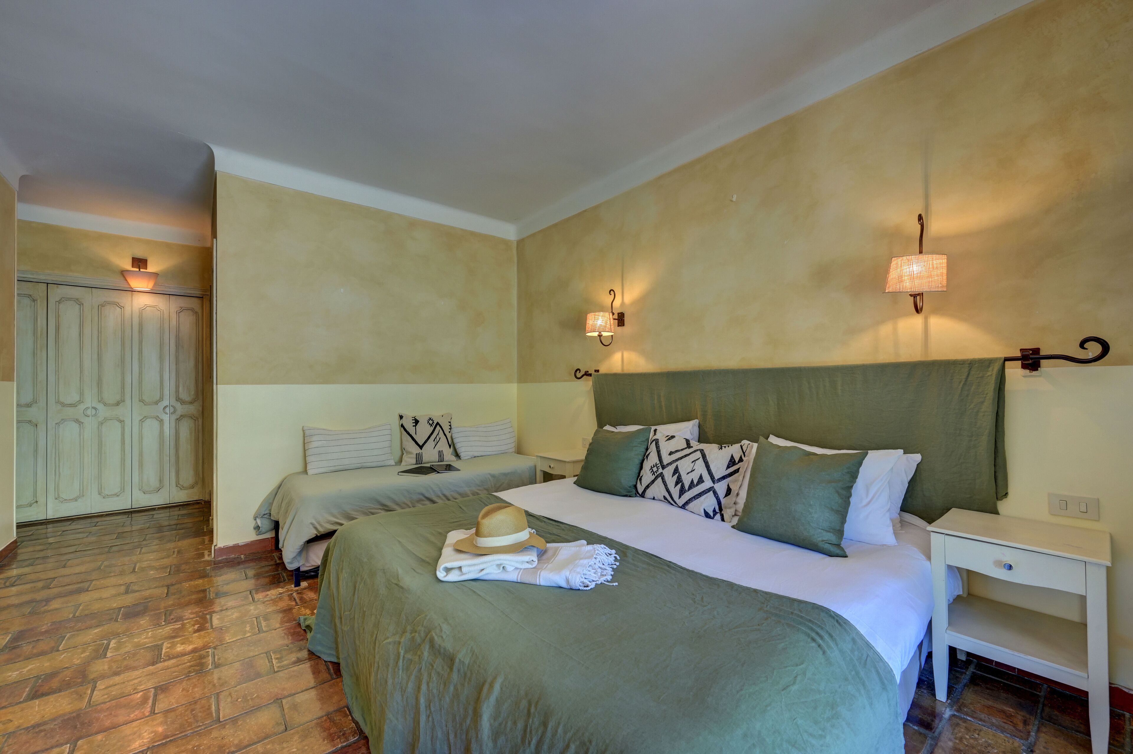 Une chambre d’hôtel avec deux lits, une armoire, une table de chevet et des lampes fixées au mur.