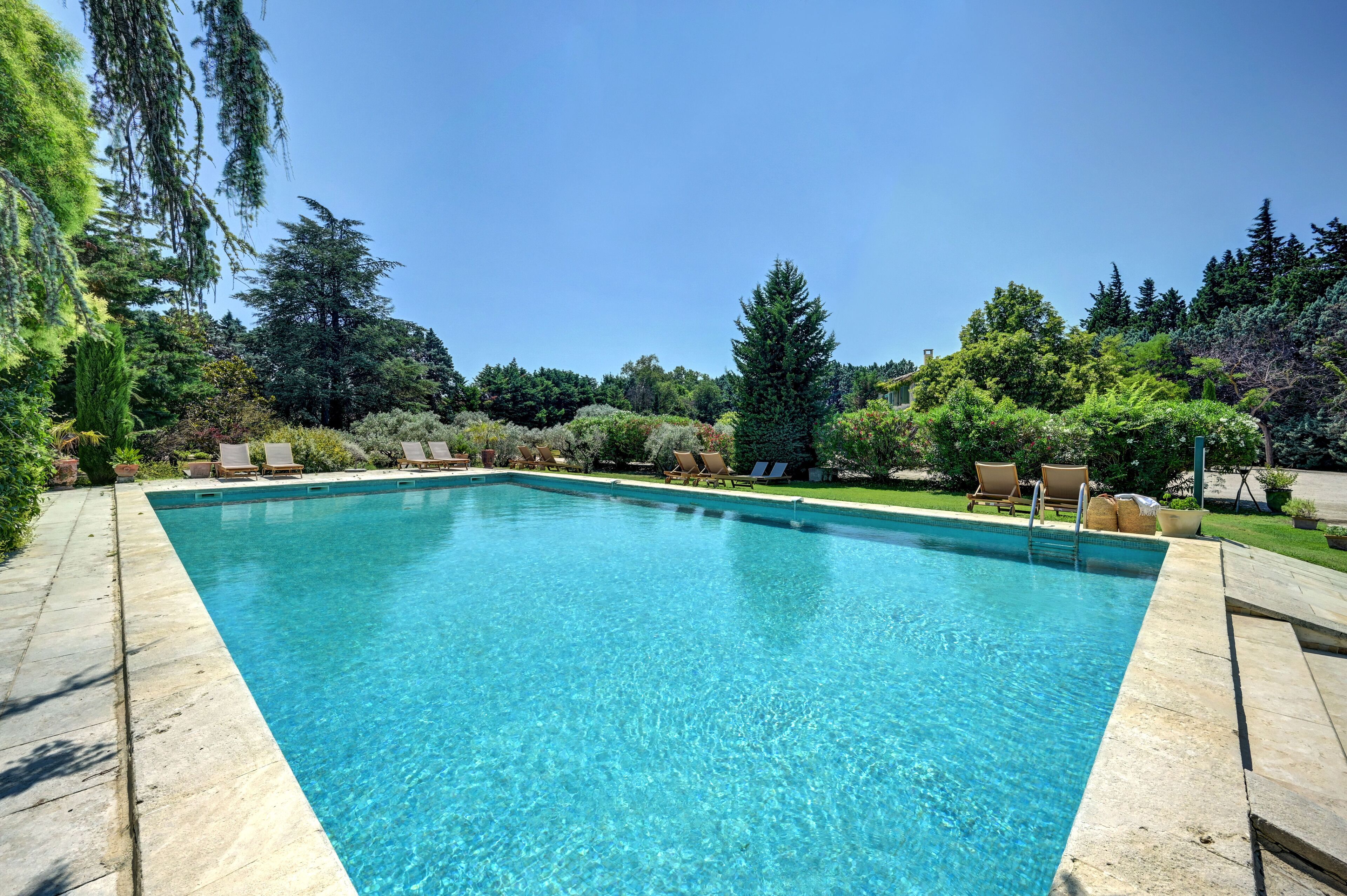 Une piscine rectangulaire à l’eau d’un bleu cristallin, entourée d’une terrasse en pierre et de chaises longues.