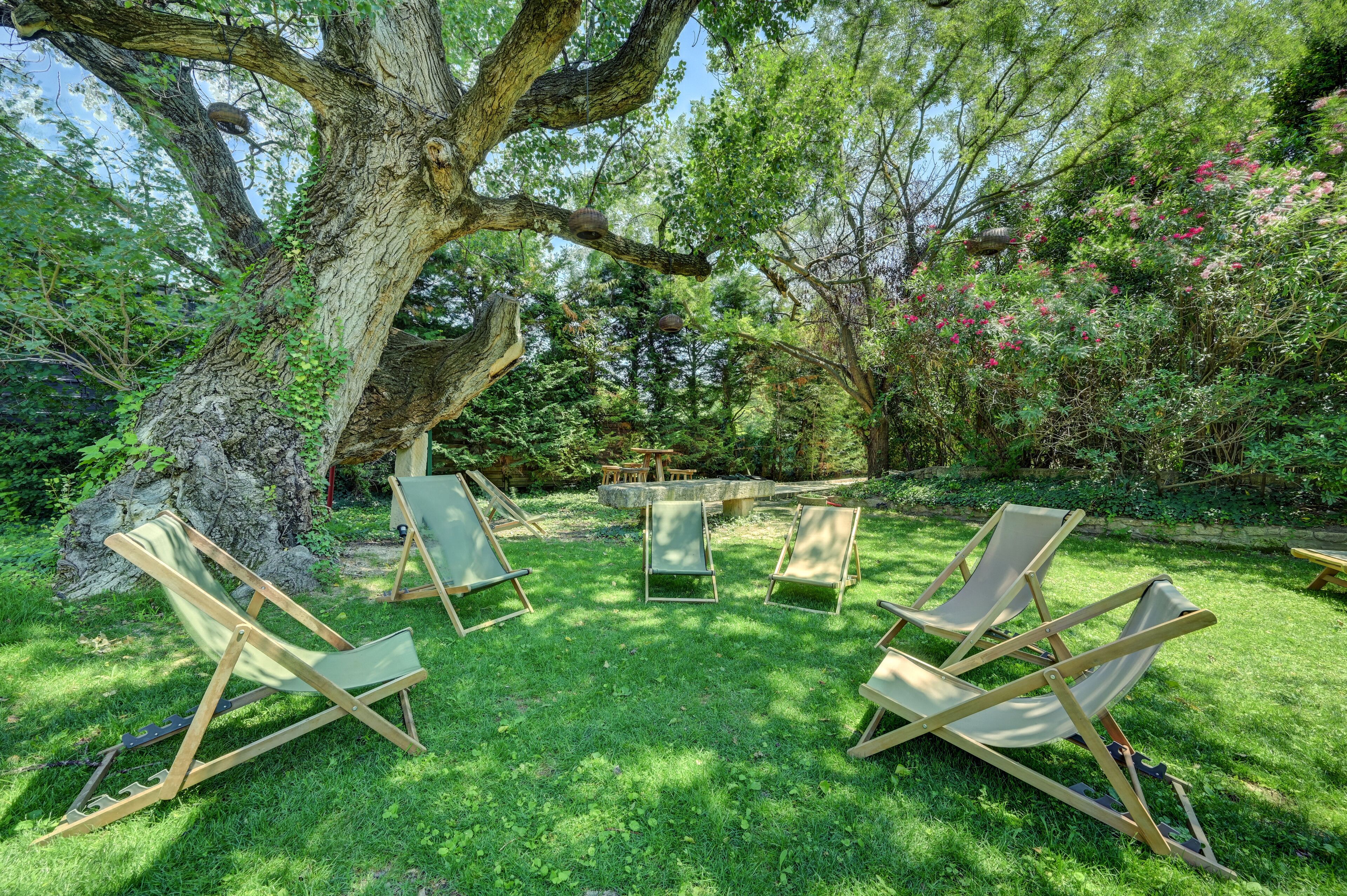 Un jardín con un árbol grande, una mesa de piedra y cuatro sillas de madera.