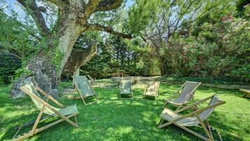 Un jardin avec un grand arbre, une table en pierre et quatre chaises en bois.