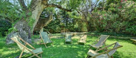 Un jardín con un árbol grande, una mesa de piedra y cuatro sillas de madera.