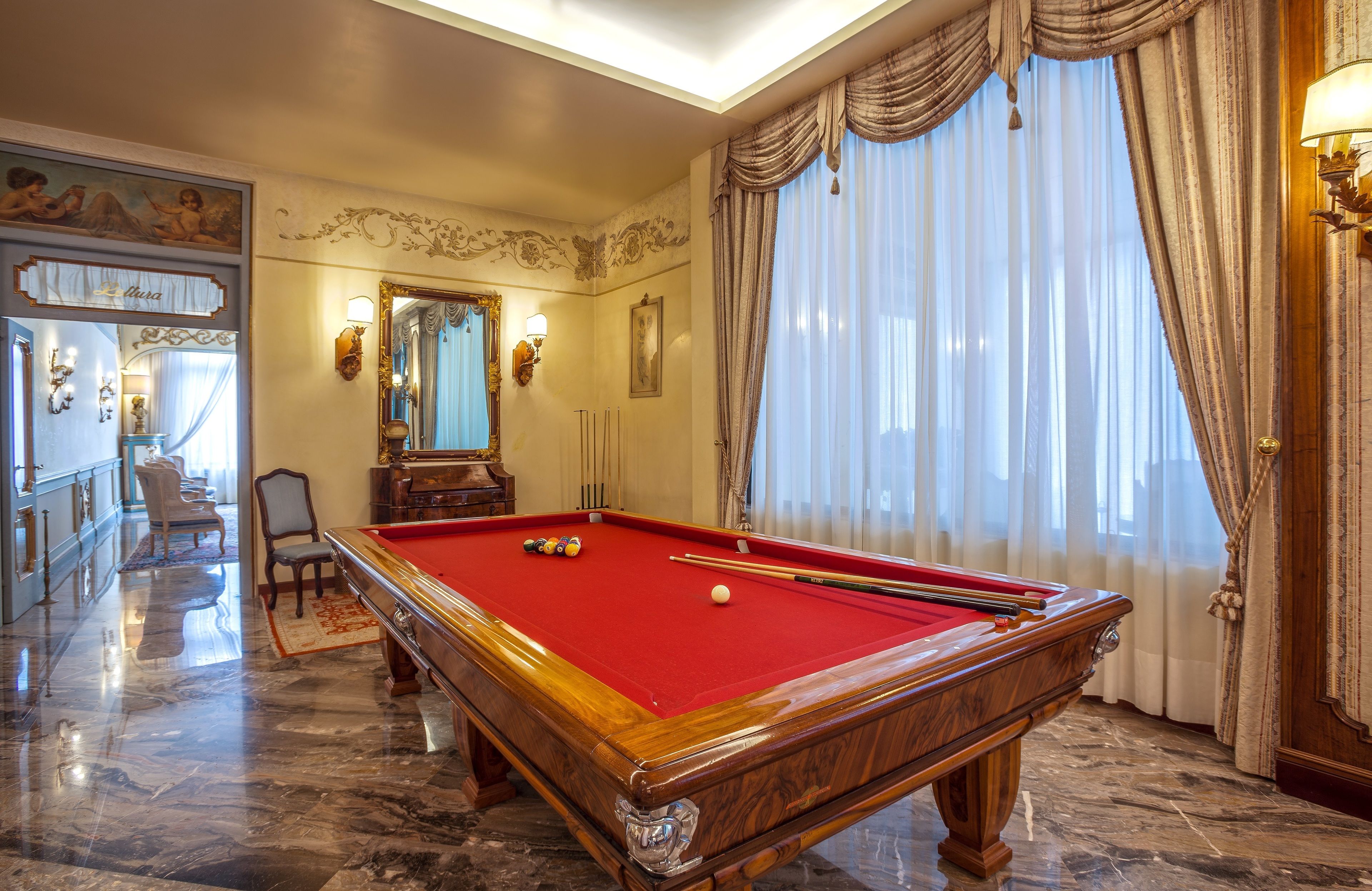 A billiards table in a room with a marble floor, a chandelier, and a large mirror.