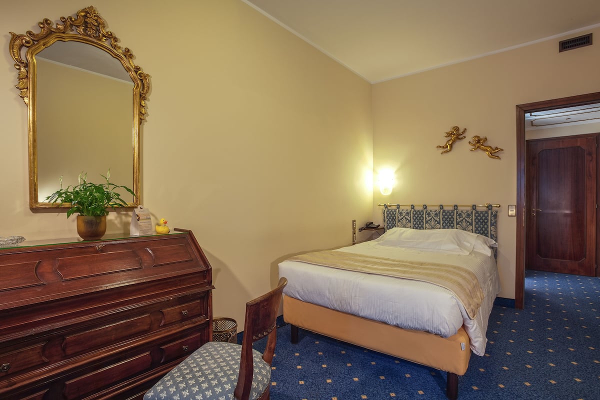 A bedroom with a bed, dresser, mirror, and a potted plant.