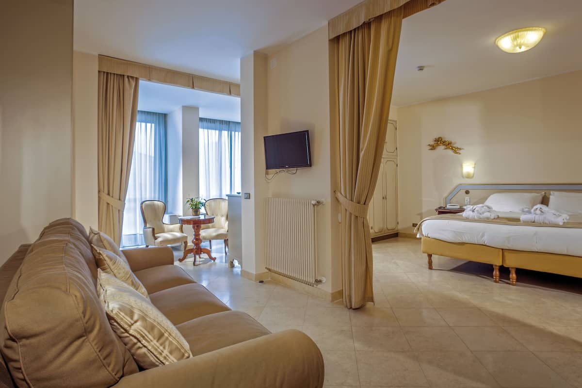 A hotel room with a sofa, a bed, a TV, and a dining area with a table and chairs.
