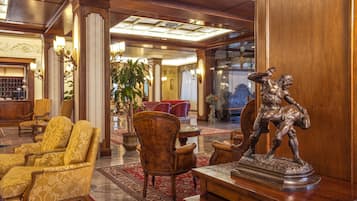 A lobby with ornate wooden furniture, a statue, and a large plant.