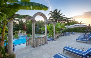 A pool area with lounge chairs and umbrellas, surrounded by greenery and architectural columns. - Hotel Abano Ritz (Abano Terme)
