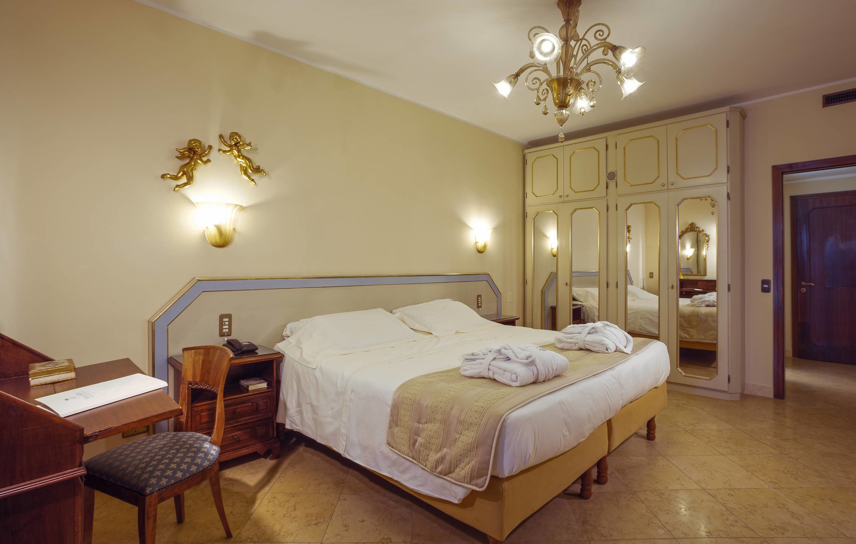 Una camera d'albergo con un letto, una scrivania, una sedia, un armadio e un lampadario.