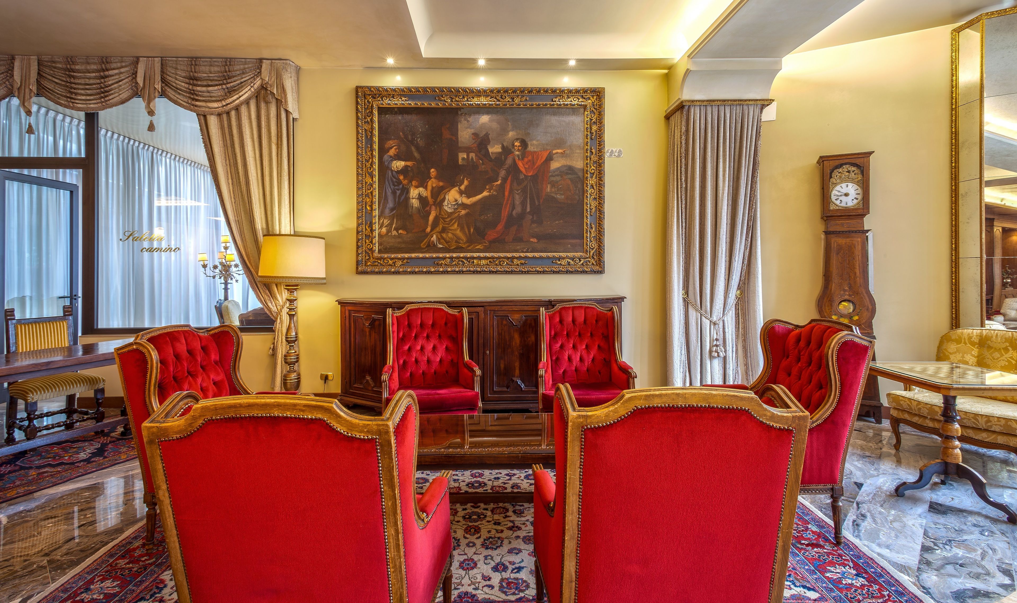 A formal dining room with red upholstered chairs, a large painting above the fireplace, and classic furniture.