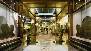 Un lobby de hotel imponente con piso reflectante, candelabros ornamentales y una zona de estar central.