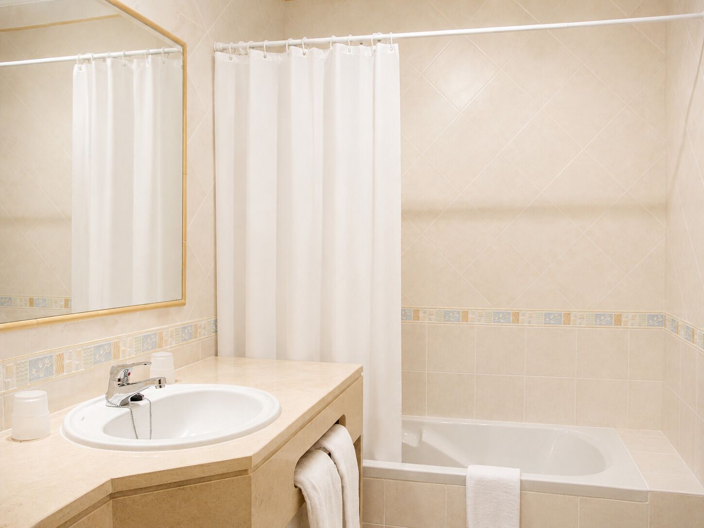 A bathroom with a sink, mirror, shower curtain, and bathtub.