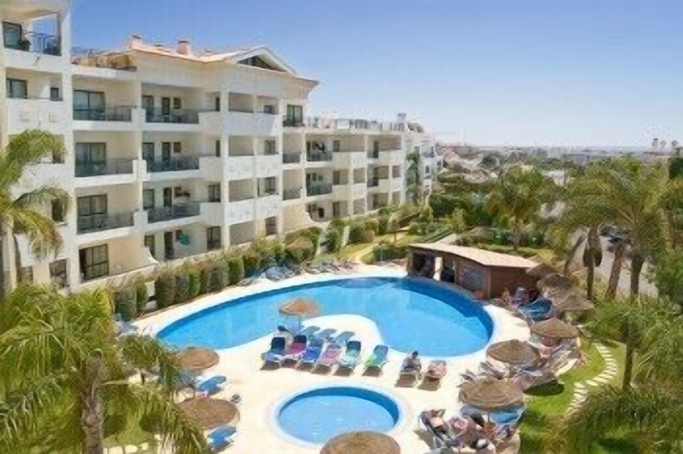 Un hotel con una grande area piscina, numerosi balconi e rigogliosa vegetazione.