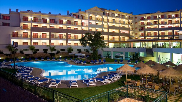 A hotel with a large swimming pool surrounded by lounge chairs and umbrellas, multiple balconies, and a well-lit facade. - Cerro Mar Atlantico & Cerro Mar Garden (Albufeira)