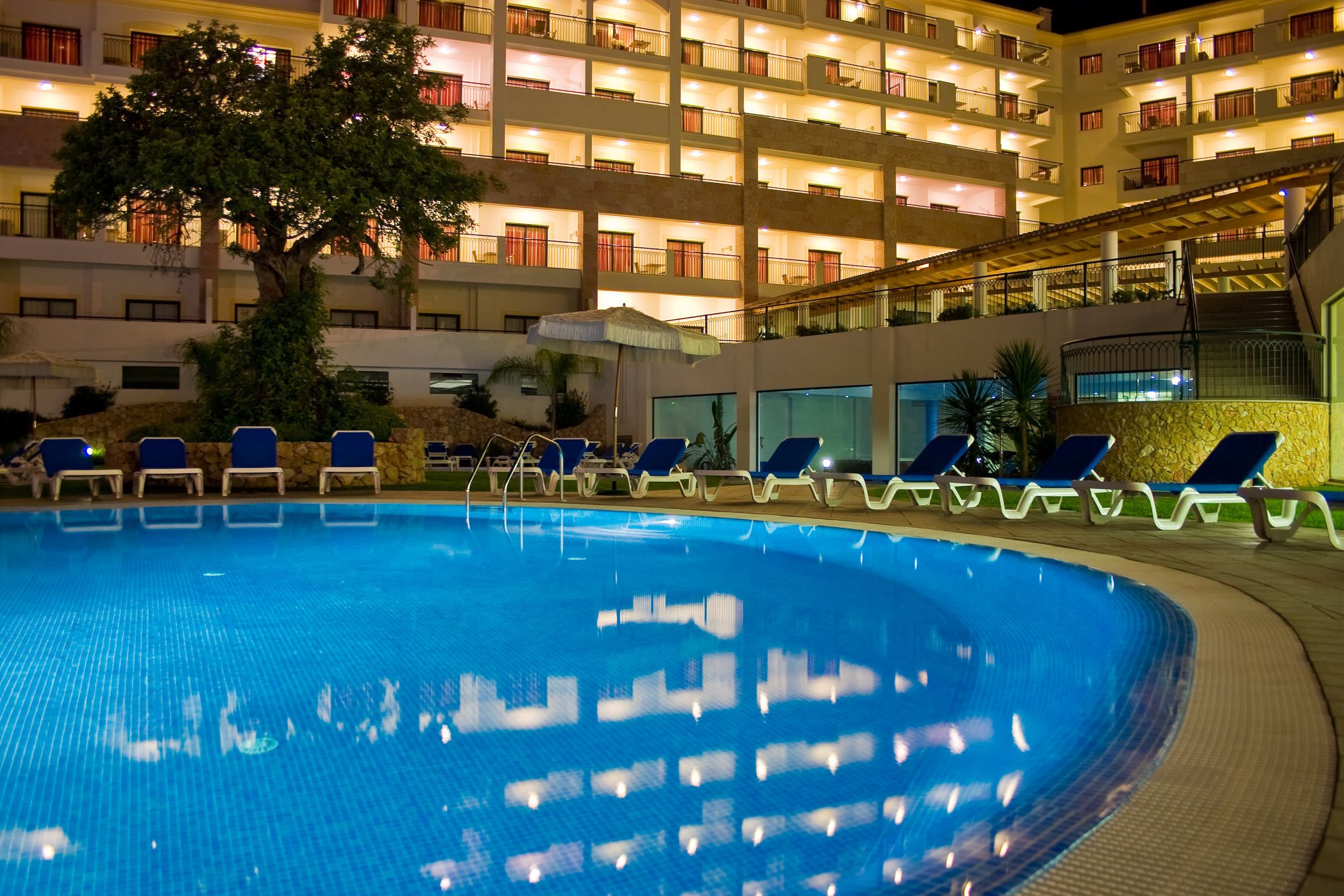 A swimming pool with lounge chairs and a building with multiple balconies in the background.