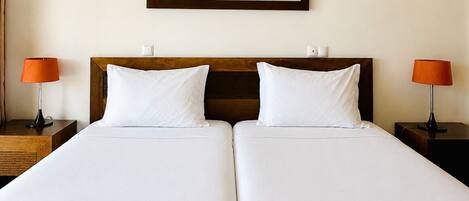 A double bed with white linens, two bedside tables with lamps, and a framed abstract painting on the wall.